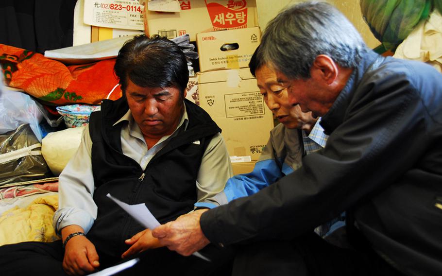 (from left to right) Jeong Ji-eun, Jang Seok Ju and Jon Chon-bong look at old aerial photographs of Wolmi Island, where they lived before the U.S. bombed the island in September 1950 to rid it of North Korean troops. The men are part of a group of former Wolmi Island residents suing the city of Incheon, South Korea, the United States and the United Nations for damages caused to their families&#39; property during the bombings.