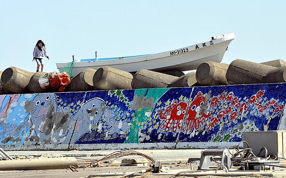 A young girl plays earlier this month next to a boat that had been beached on a seawall in Misawa City's port when a tsunami wave ripped through the area, gutting building and washing out roads.