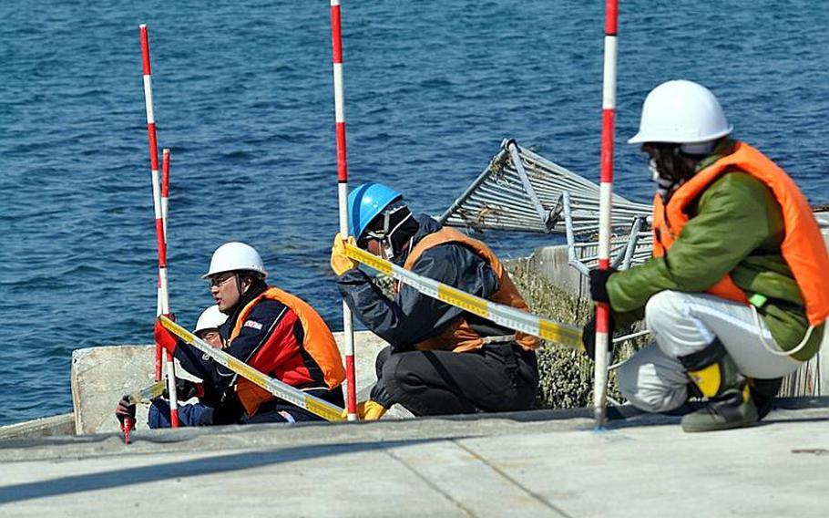 Construction workers measure the level of damage at the Misawa City port earlier this month. The port was slammed with a huge tsunami wave on March 11.