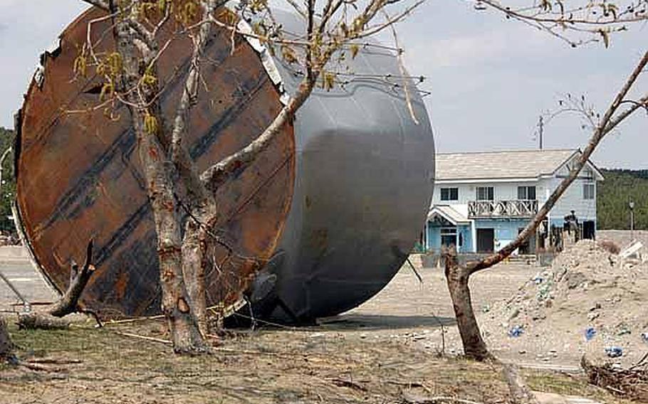 A fuel tank sits on its side Tuesday, washed into this field when a March 11 tsunami battered the Misawa City port. A partially gutted building can be seen in the background.