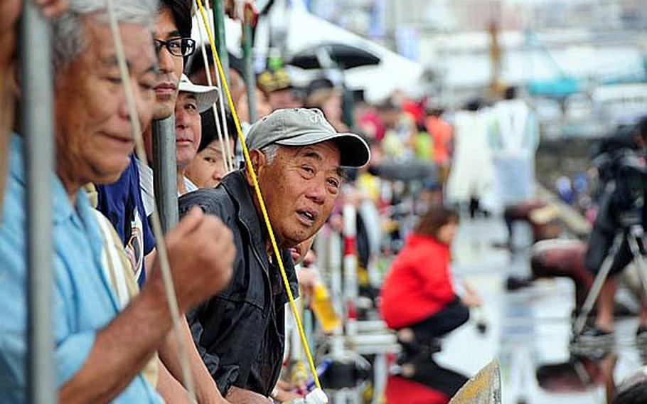 A spectator peers out from underneath a tent at the 37th annual Naha Hari dragon boat races held Thursday in Okinawa's Naha Port. Despite the on-again-off-again rain, many people turned out to watch the dragon boat teams battle it out in the port.
