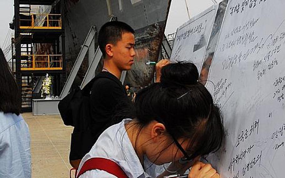 Participants in USFK's Good Neighbor English Camp write messages of condolence for the sailors who died in March 2010 when their ship, the Cheonan, was sunk by a North Korean torpedo. Behind them is the wreckage of the ship, now on display at a South Korean naval base.