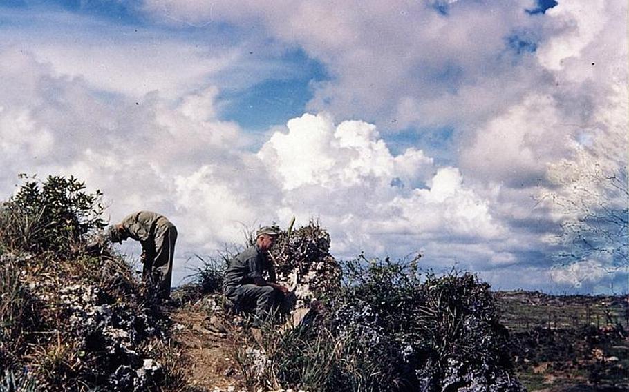 Two servicemembers give a safety check of a path from atop a ridge in the southwestern tip of Okinawa for a visit of Army Lt Gen. Simon B. Buckner, Jr., who led Army and Marine troops in the Battle of Okinawa. Shortly after taking this photo, Buckner was killed when fragments of an artillery shell struck him in June 18, 1945, five days before the battle ended on the island.