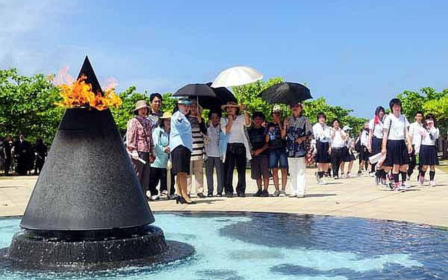 A tour guide explains to listeners about the 'Flame of Peace,' memorial, which is at the end of the 1,200 granite walls bearing the names of 240,000 military and civilians who died during the Battle of Okinawa. The top of the metal cone is lit at all times and water tumbles from the base of the cone and fills a circular pool with a map of the Pacific at the bottom.