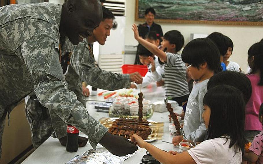 Spc. John Anderson "sells" a meat kebab to a Taesongdong Elementary School student during the school's market day, when students practice buying and selling goods in English. U.S. troops stationed at the Joint Security Area visit the school once or twice a week to help teach English.