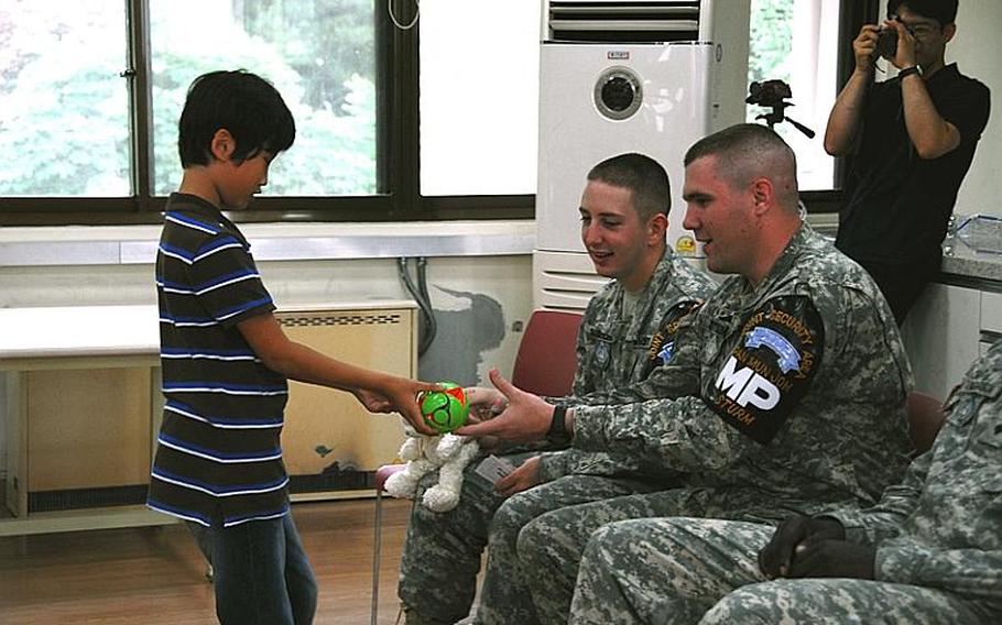 Spc. Joshua Sturn, right, "buys" a toy from a Taesongdong Elementary School student during the school&#39;s market day, when students practice buying and selling items in English. To his left is Pvt. Bradley Chamberlain. Both are stationed in the Joint Security Area.