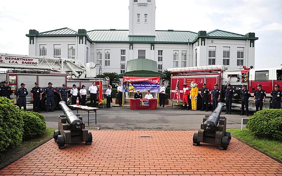 Flanked by the entire Sasebo Navy Base fire department, Commander Fleet Activities Sasebo Capt. Charles Rock, left, sits with Installation Fire Chief Gerald Clark and signs a proclamation Tuesday morning in front of the captain's office to declare Oct. 9-15 Fire Prevention Week at the base. In addition to fire drills and raising awareness with children on the base, the Sasebo department also does outreach with local Japanese school children. Fire Prevention Week is being observed nationwide this week in the U.S. and in DODEA schools around the globe.