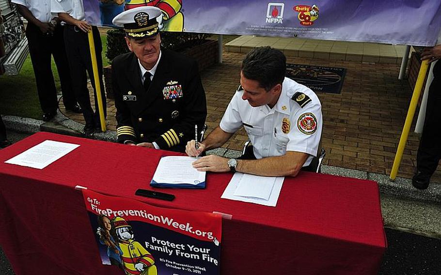 Commander Fleet Activities Sasebo Capt. Charles Rock, left, sits with Installation Fire Chief Gerald Clark and signs a proclamation Tuesday morning in front of the captain's office to declare Oct. 9-15 Fire Prevention Week at the base. In addition to fire drills and raising awareness with children on the base, the Sasebo department also does outreach with local Japanese school children. Fire Prevention Week is being observed nationwide this week in the U.S. and in DODEA schools around the globe.