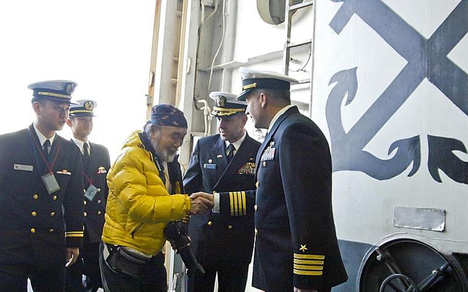 Shima Takashi, in yellow, is greeted Dec. 13, 2011, by Capt. David Fluker, center, skipper of the Wasp class multipurpose amphibious assault ship USS Essex, and Capt. Daniel Dusek, right, the ship's executive officer, as he arrives at the ship to present his most recent work for display. The 68-year-old  from Wakayama prefecture painted the Essex in elaborate detail to thank the U.S. military and the ship&'s crew for their participation in Operation Tomodachi.