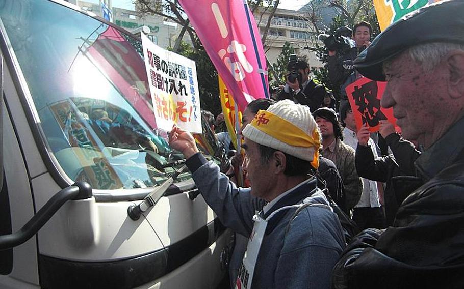 An anti-military activist flashes a card Dec. 27, 2011, that reads "We won't let you deliver an environmental report to Governor." About 100 protesters surround a carrier service van that carries the report at the prefectural government office, sending the vehicle away without making delivery.