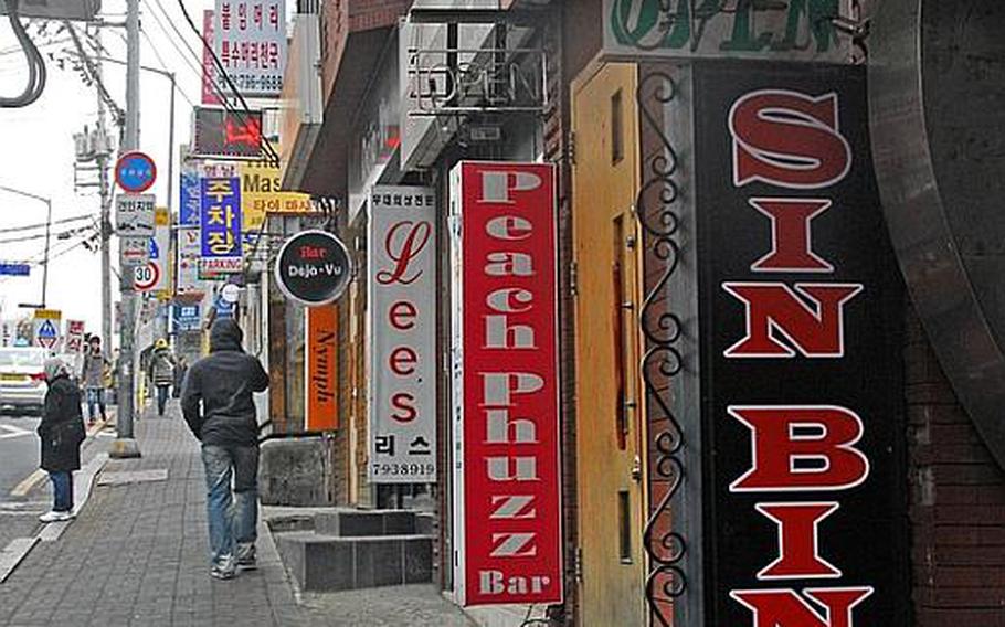 A man walks down a sidewalk in front of a row of bars in Itaewon, Korea.