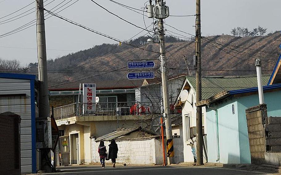 Two girls walk down a street in the main village of Yeonpyeong Island. Behind them, a scarred mountainside hit by North Korean artillery fire in November 2010 is marked by rows of debris.
