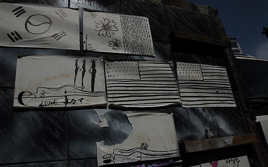 Drawings of American flags, the South Korean flag, and people lying down are posted on a wall on Hooker Hill, next to the site where the Tiger Tavern once stood.