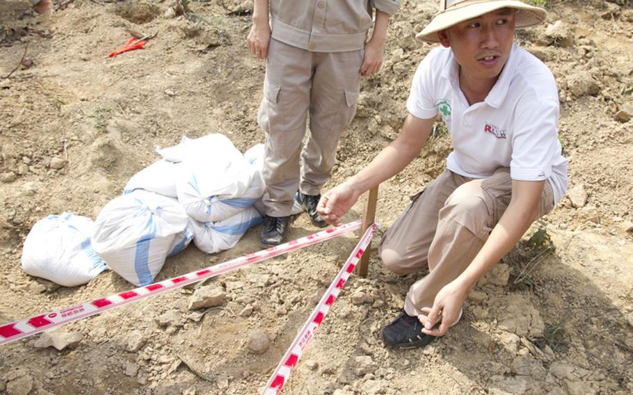 Dinh Ngoc Vu, the explosive ordnance disposal operations manager for Project Renew, shows a cluster bomb found at a cleanup site a few miles outside the town of Dong Ha, Quang Tri Province. The bomb, appearing almost identical to a rock, is the round object in front of his left foot just over the safety tape.