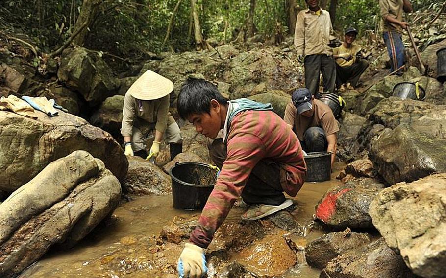 Local Vietnamese men and team members from the Joint POW/MIA Accounting Command use their hands to remove sediment from a stream bed in Binh Dinh Province, Vietnam March 14, 2012. The sediment will be screened and carefully inspected for any sign of osseous material or other evidence that can help identify a soldier missing from the Vietnam Conflict. JPAC's mission is to conduct global search, recovery and laboratory operations to identify unaccounted-for Americans from past conflicts in order to support the Department of Defense's personnel accounting efforts.
