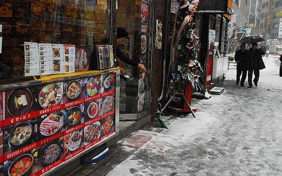 A woman tosses salt outside the entrance of a restaurant near the Far East District Compound on Dec. 5, 2012, to prevent icing on the sidewalk. Snow began to fall heavily in Seoul around noon, causing slick sidewalks and roads and traffic jams.