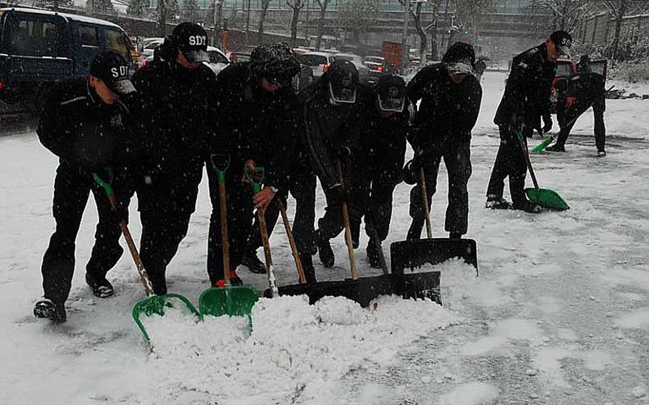 South Korean troops work in unison to shovel snow from a sidewalk in front of the Ministry of National Defense complex, not far from the entrance to U.S. Army Garrison Yongsan. Dec. 5, 2102, marked the first significant widespread snowfall of the season in South Korea, and additional snow was expected on the coming Friday and throughout the weekend.