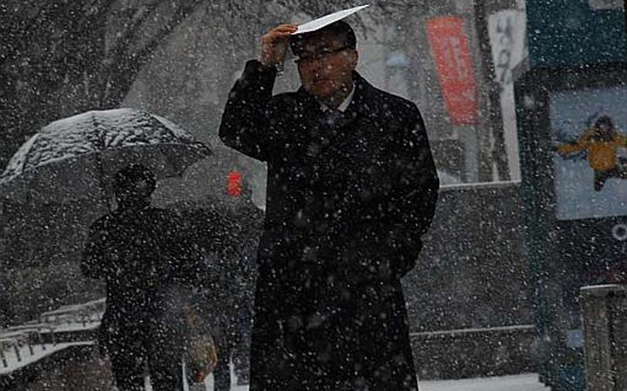 A South Korean man covers his head as he walks through snow near the Far East District Compound on the afternoon of Dec. 5, 2012.