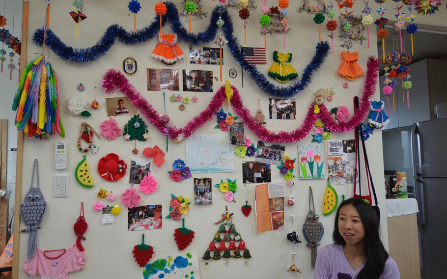A wall adorned with pictures and gifts from U.S. military families is a prominent part of the community room at the Terauchi No. 2 temporary housing development in Minamisoma, Japan. Seated is Masako Sullivan, a Navy spouse who has been instrumental in helping military families provide supplies and emotional support to the 40 households living there.