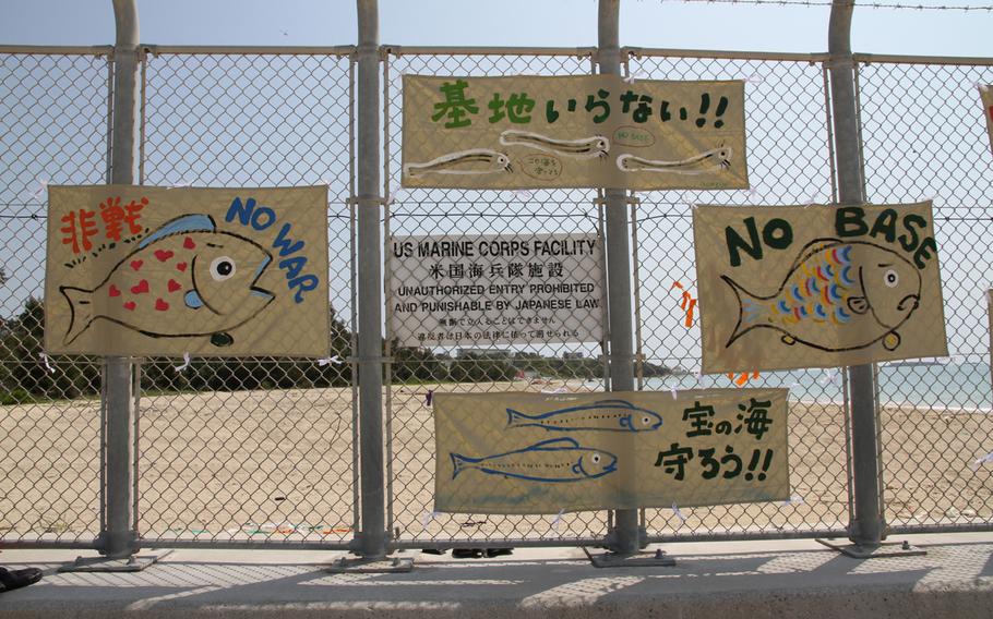 In this file photo from mid-April 2014, signs adorn a barbed-wire fence leading to Camp Schwab, Okinawa, during a protest commemorating the 10-year anniversary of the start of the 1st sit-in protest seeking to block the expansion of the base.