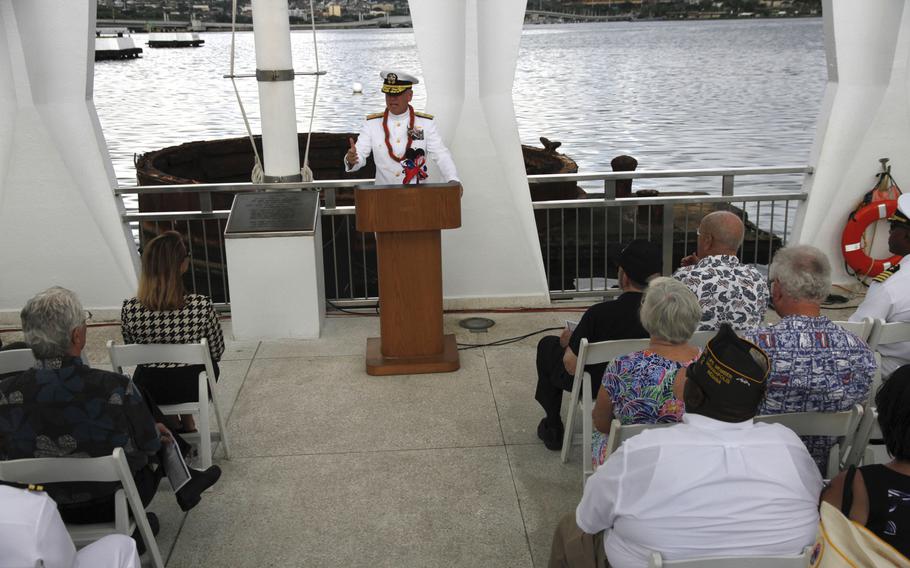 Rear Adm. Rick Williams, commander of Navy Region Hawaii and Naval Surface Group Middle Pacific, speaks to guests during the dedication of a the USS Arizona Memorial Wall in Honolulu on Veterans Day. Jutting up through the water behind him is the base of the sunken Arizona's gun turret.