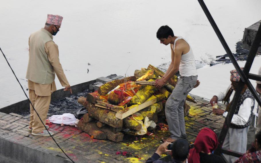 A son prepares to set the body of his recently deceased father on fire during a cremation ceremony beside the Bagmati River, Nepal. A Hindu priest covers the body in marigolds, barley, rice, and yellow and red powder before the cremation.