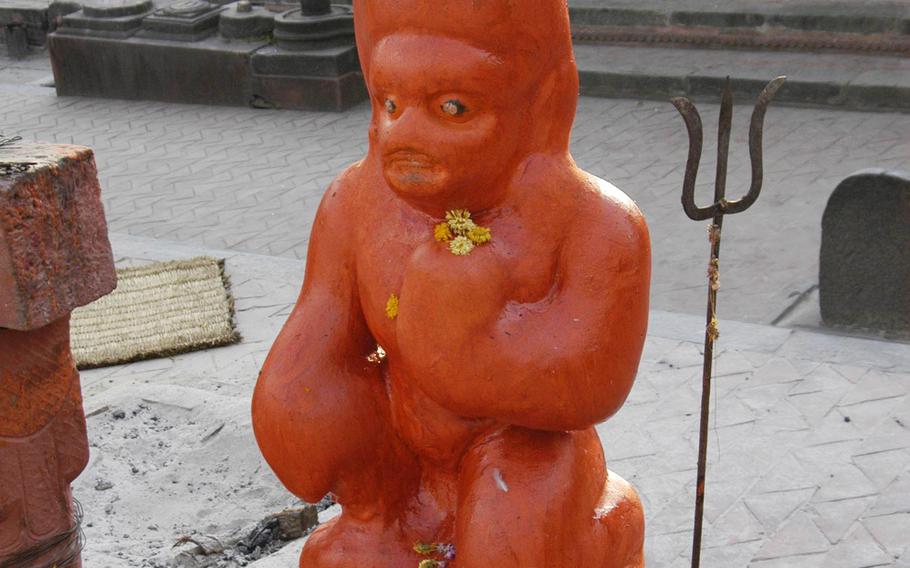 A statue representing a monkey god watches over cremations beside the Bagmati River, Nepal.