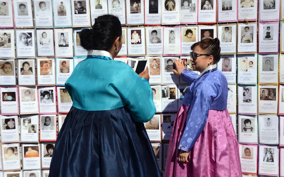 Sook Hee Scheibner, right, who was adopted from South Korea as a toddler, is photographed by a friend while pointing to a photo of herself as a baby on a memorial wall in Paju, South Korea, Sept. 12, 2018.