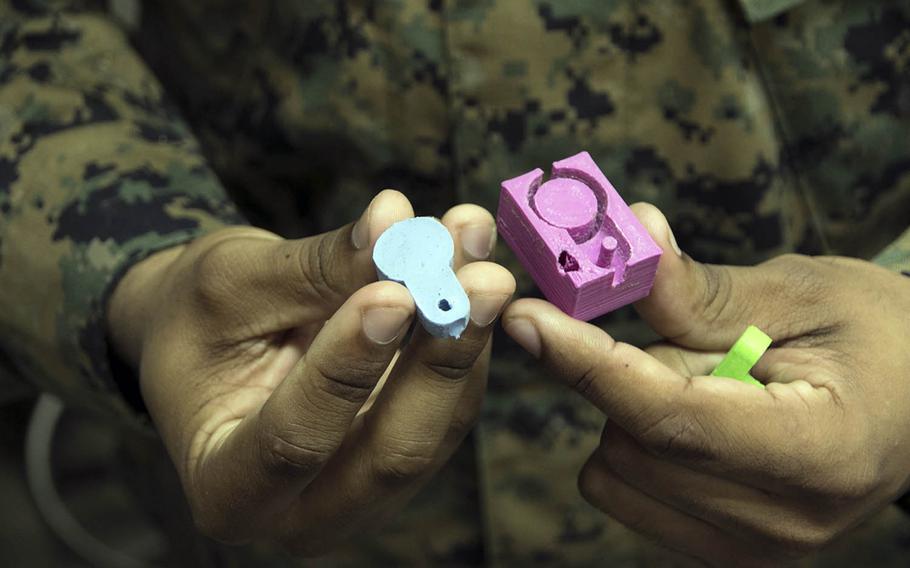 Marine Sgt. Adrian Willis of the 7th Communications Battalion on Sunday, Feb. 5, 2019, holds a radio dust boot cover, left, and a mold for the piece that was made using the unit's 3D printer.