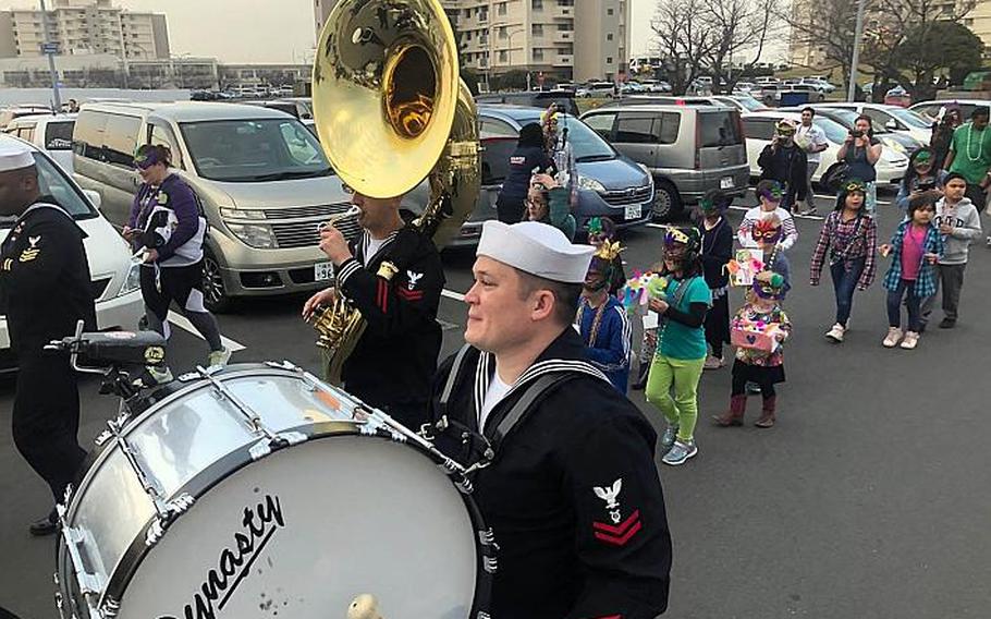A Navy band leads a foot parade through the commissary parking lot during the USO Mardi Gras celebration at Yokosuka Naval Base, Japan, Tuesday, March 5, 2019.