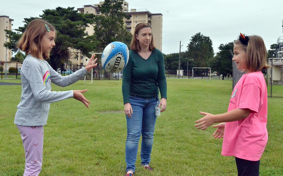 Teacher Katherine Ericson watches students Katie Petty, left, and Emery Horne toss a rugby ball outside Yokota West Elementary School at Yokota Air Base, Japan, Friday, Oct. 18, 2019. Ericson brought a group of English rugby players to the school to teach about the challenges faced by those with visual impairments.