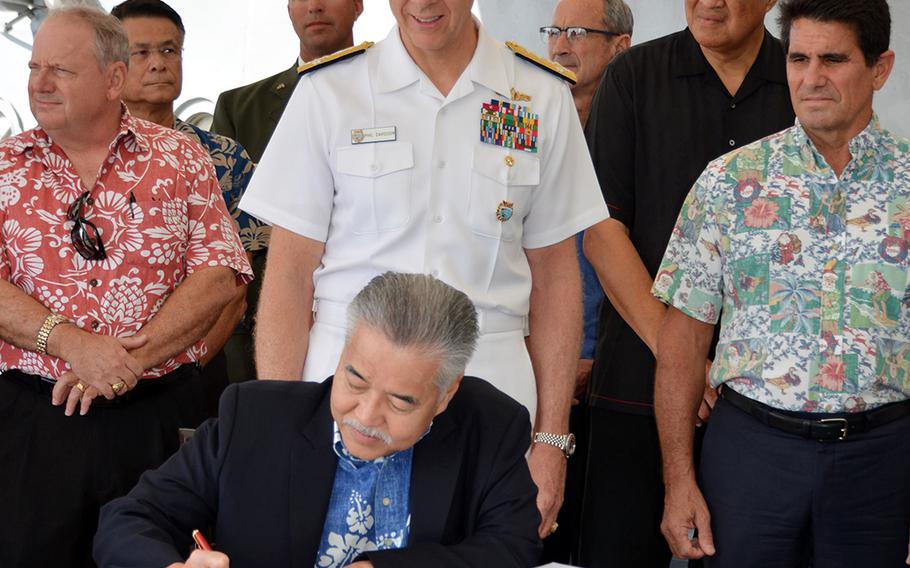 Hawaii Gov. David Ige signs a proclamation while seated on the deck of the Battleship Missouri Memorial, Wednesday, Dec. 18, 2019, announcing the membership of the committee overseeing next year's 75th anniversary of the end of World War II. Ige and U.S. Indo-Pacific Command head Adm. Phil Davidson, standing behind the governor, are honorary committee co-chairs.