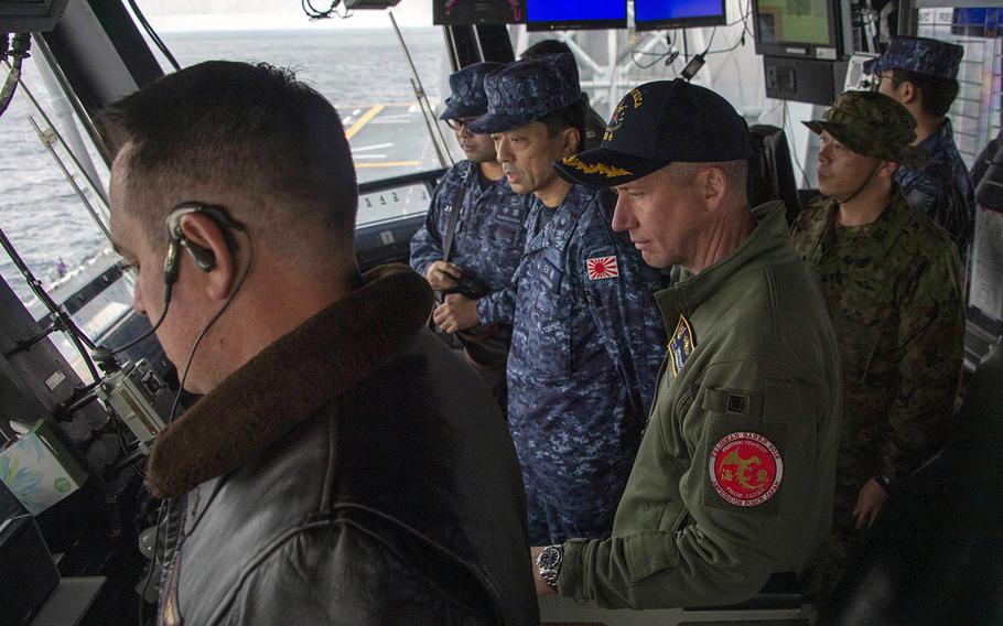 Capt. Luke Frost, center, commander of amphibious assault ship USS America, and Japan Maritime Self-Defense Force Rear Adm. Shirane Tsutomu, commander, JMSDF Mine Warfare Force, watch flight operations in America's primary flight control center in the East China Sea on Jan. 13, 2020.