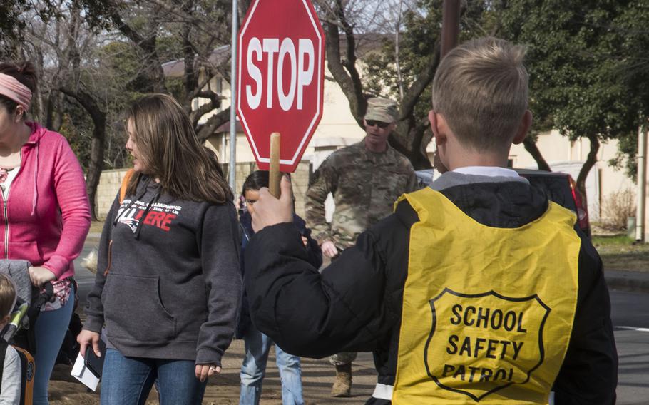 A crossing guard stops traffic for students near Joan K. Mendel Elementary School at Yokota Air Base, Japan, Friday, Feb. 28, 2020.