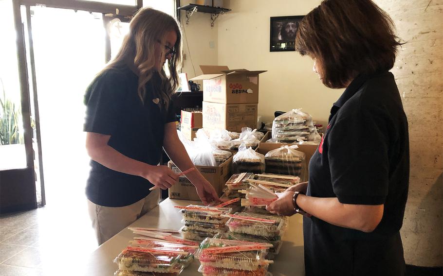 Help Oki volunteers Aubrie Owens, left, and Yuko Nesbitt prepare bento lunch boxes for needy Okinawans, Thursday, March 12, 2020.