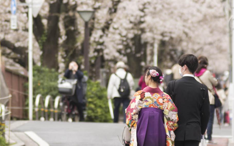 People stroll near the Meguro River in central Tokyo to see the cherry blossoms, Monday, March 23, 2020.