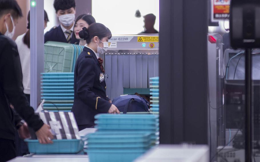 Travelers pass through a security checkpoint at Haneda International Airport in Tokyo, March 18, 2020.