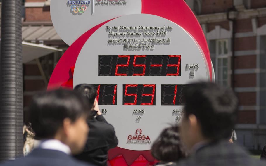 Commuters stop outside Tokyo Station to check out a clock counting down to the Summer Olympics, Wednesday, March 25, 2020. The display was changed to show the current date, 25-3, following a decision to postpone the event because of the coronavirus.