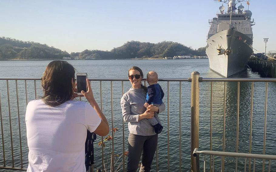 Ashton Andrews and her son, Thomas, pose for a photo with their husband and father, Lt. Cmdr. Ryan Andrews, waving far in the distance on the USS Antietam, at Yokosuka Naval Base, Japan, Thursday, March 26, 2020.