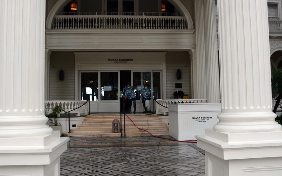 Wearing protective masks, employees on March 31, 2020, clean and disinfect the main entrance of Moana Surfrider hotel, which like most hotels on Waikiki Beach has suspended operations in the wake of state and city shelter-in-place orders.