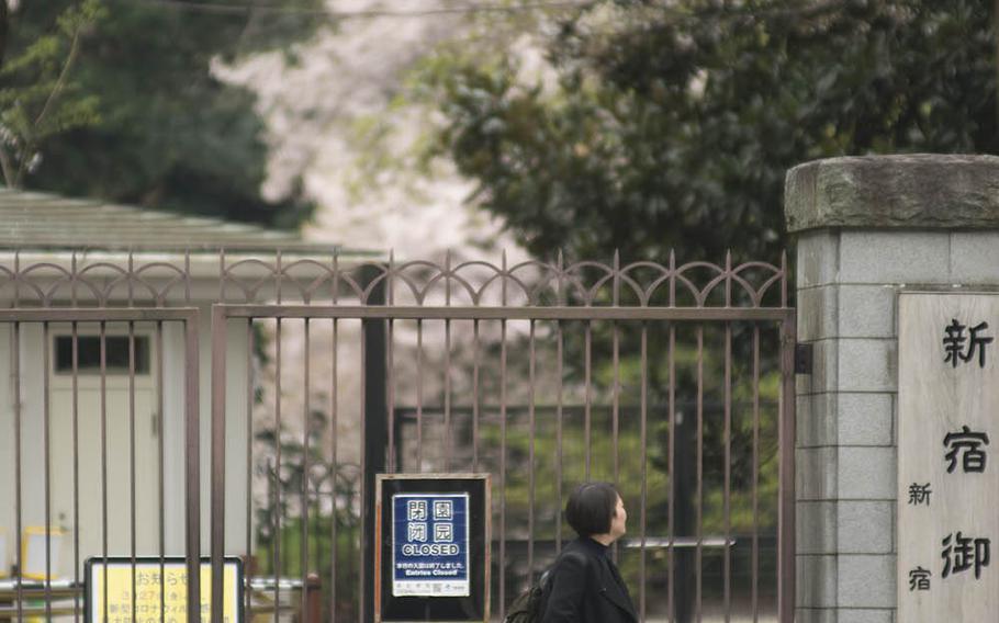 A woman strolls by the entrance to Shinjuku Gyoen, a popular Tokyo park that has been closed because of the coronavirus pandemic, Monday, March 30, 2020.
