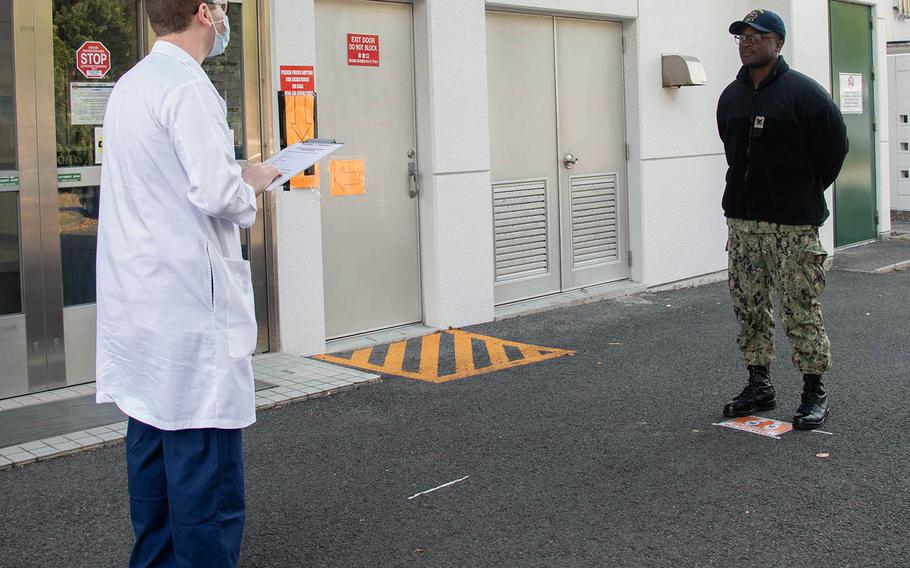 Hospital corpsman Nicholas Bond, left, questions fellow Petty Officer 3rd Class Darien Huggins outside the health clinic at Sasebo Naval Base, Japan, April 2, 2020.