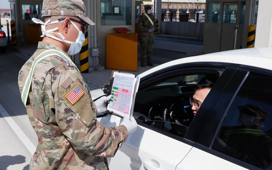 A soldier with the 2nd Armored Brigade Combat Team, of Fort Riley, Kan., interviews someone coming through the Adams Gate at Camp Humphreys, South Korea, for indicators of coronavirus on April 7, 2020.