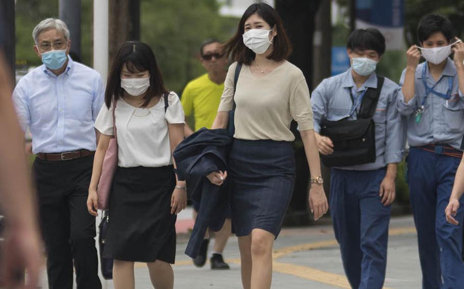 Commuters cross a roadway near Kudanshita Station in central Tokyo, July 27, 2020.