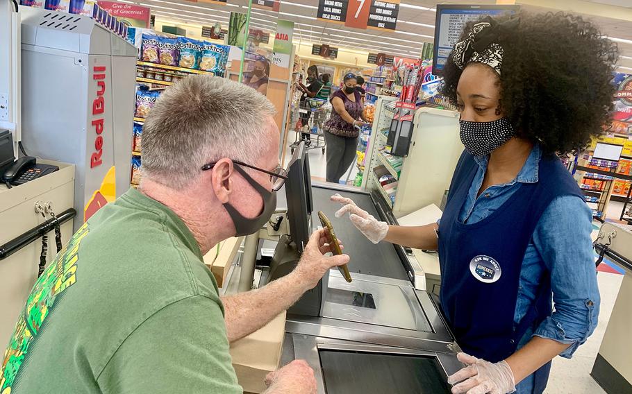 Samaritan Shopper Program volunteer Kim McCann holds up his phone so the quarantined person he shopped for can tell her credit card number to a commissary cashier at Yokosuka Naval Base, Japan, Aug. 4, 2020. 