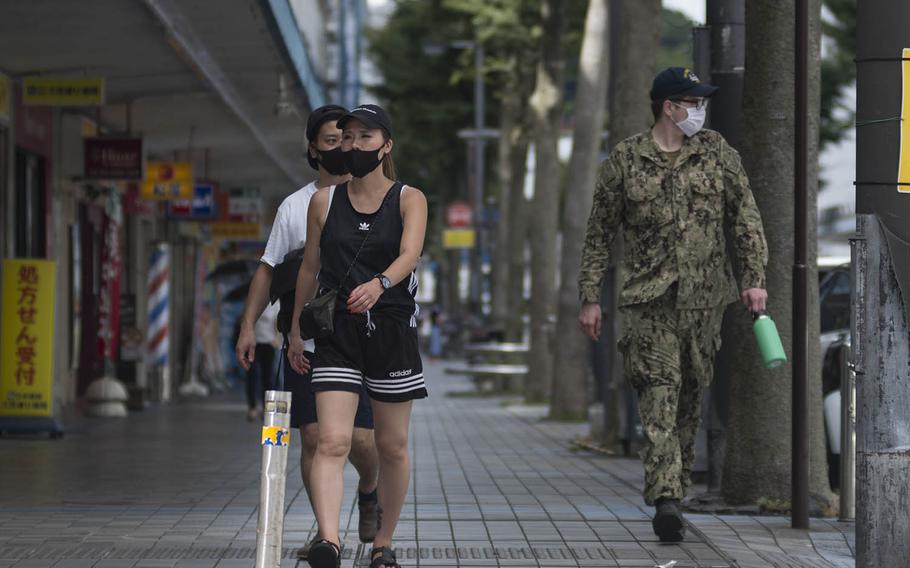 A U.S. Navy sailor and locals wear masks as they stroll down a walkway in Yokosuka, Japan, Thursday, Aug. 27, 2020. 