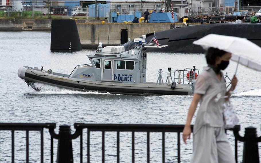 A woman walks by a U.S. Navy police boat patrolling near Yokosuka Naval Base, Japan, Aug. 27, 2020.