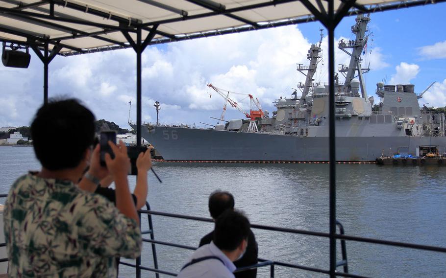 People snap photos of the USS John S. McCain as a tourist boat cruises past Yokosuka Naval Base, Japan, Aug. 27, 2020. 