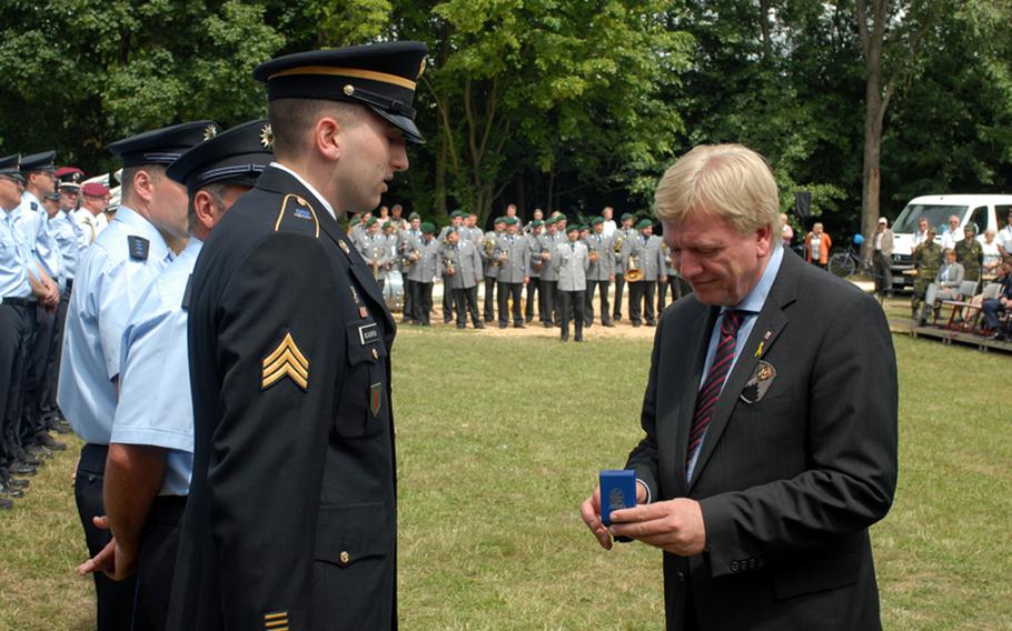 Sgt. John McCaughrean listens to Hessen Minister President, Volker Bouffier, before being presented with the German state's medal for civil courage.  In front of hundreds of spectators at this year’s Hessentag festival in Oberursel, it was a thankful German government that recognized Sgt. John McCaughrean for coming to the aid of wounded victims of a serious car accident and helping to nab two men who tried to flee the scene.