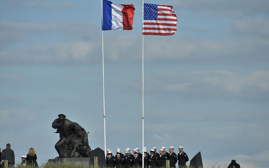 Sailors standby at the World War II Navy memorial at Utah Beach, Normandy before Adm. Jonathan Greenert, the Chief of Naval Operations, re-enlists a sailor during the 70th anniversary D-Day commemorations, June 5, 2014.